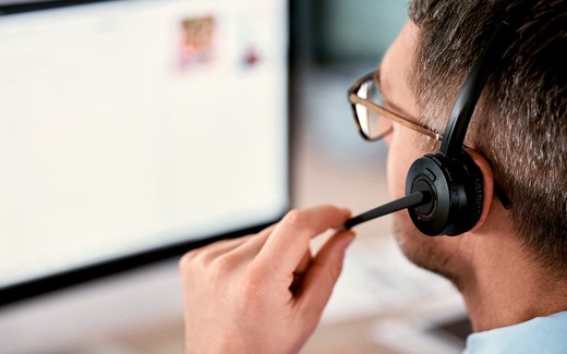 A man in a headset at a screen, adjusting the microphone.