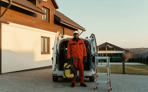 A technician at the open back of a work van outside a house.