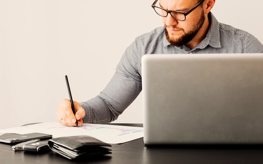 A man at a desk with a laptop, a folder and a pen.