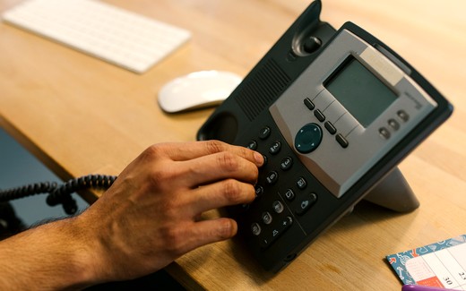 A hand on a desk phone in a small office.