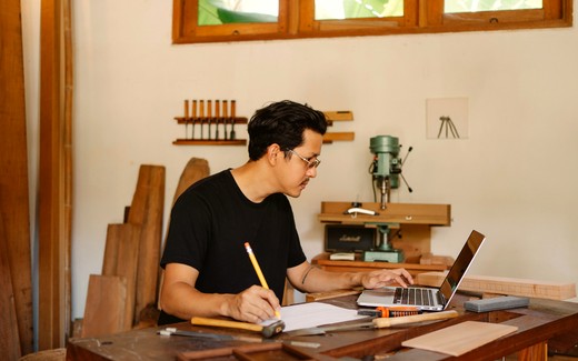A tradesman working at a laptop on his workshop bench.