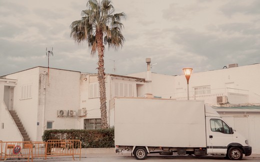 A white van parked by a pale building under palms in morning light.