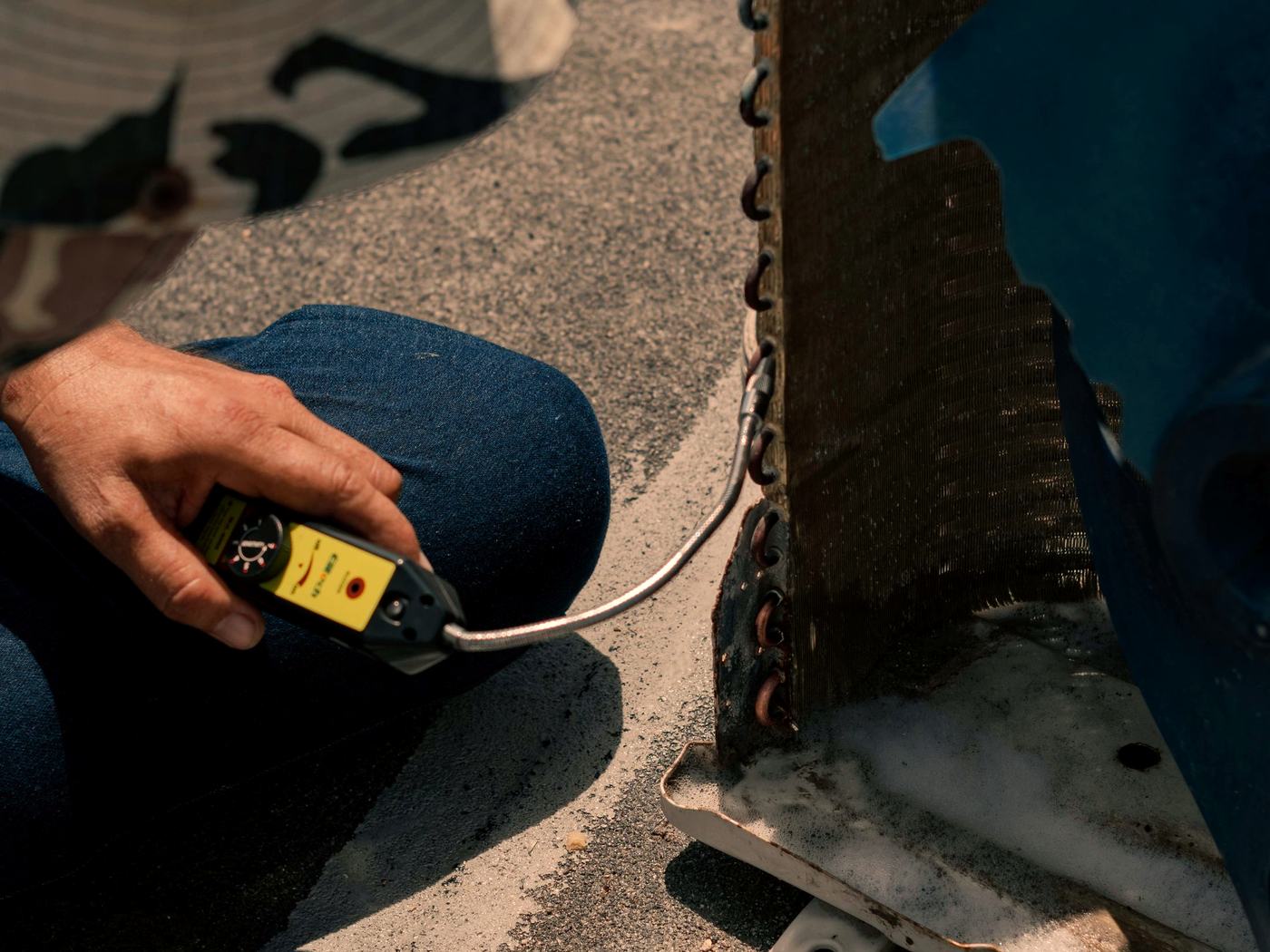 A technician taking a reading at an outdoor condenser coil in full sun.