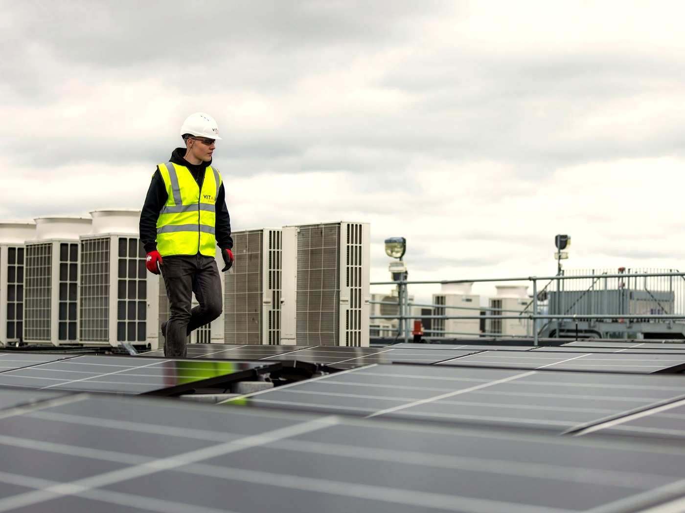A technician on a flat roof beside a run of packaged units.